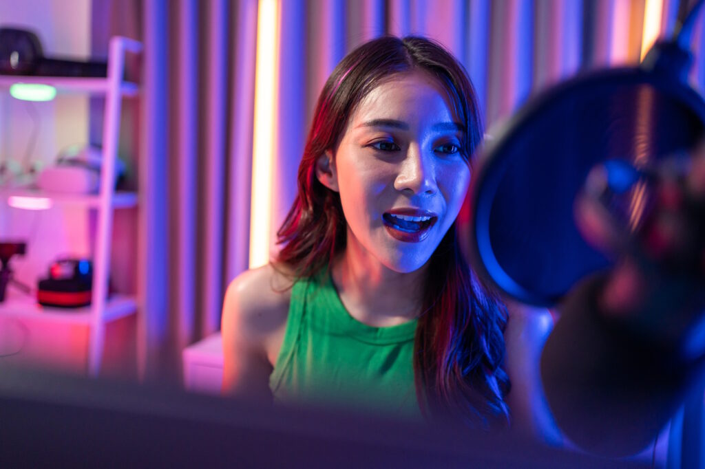 Female podcast creator recording a podcast intro in a home studio with vibrant neon lighting, showcasing the energy of engaging podcast intros.