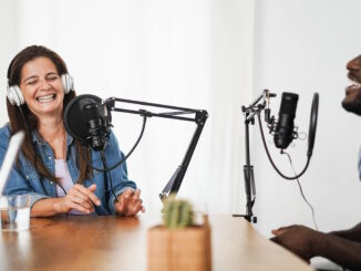 A joyful woman in a denim shirt laughing while recording a podcast with a male co-host, showcasing the lively dynamics of creating characters in podcasts.