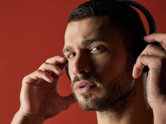 A man intently adjusts his headphones, his expression reflecting the tension and focus associated with building suspense in audio narratives